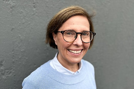 En närbild på leende person i ljusblå tröja, glasögon och mörkt hår.