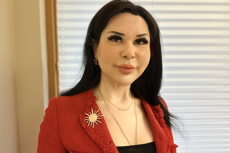 En mörkhårig person i röd kavaj tittar in i kameran