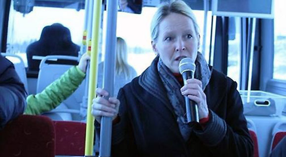 En kvinna som står i en buss och talar i mikrofon