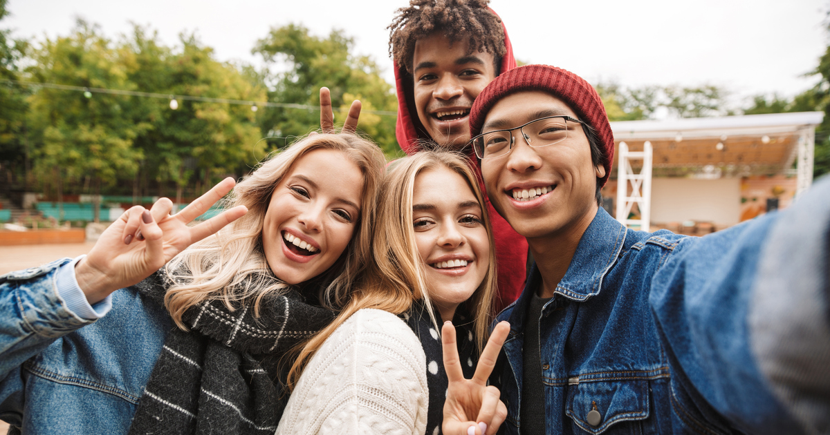 Fyra leende ungdomar som tar en selfie i utomhusmiljö.