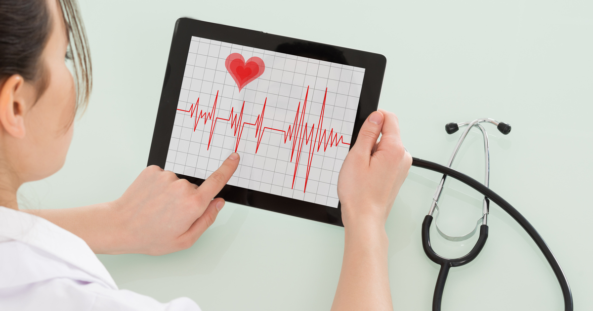 Närbild av kardiolog som analyserar hjärtslag på en läsplatta.