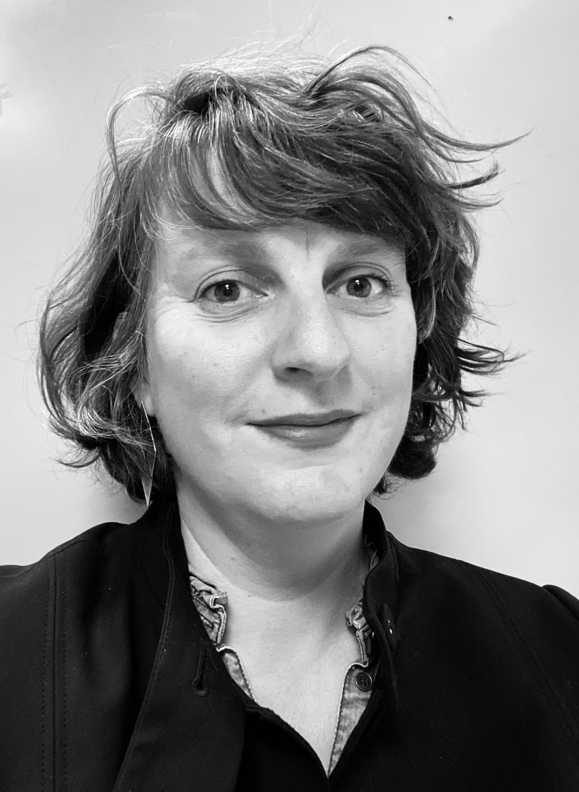 Svartvitt porträtt av en person med halvkort hår, läppstift och en tatuering som syns på ena sidan av halsen ur kragen på en svart blus.