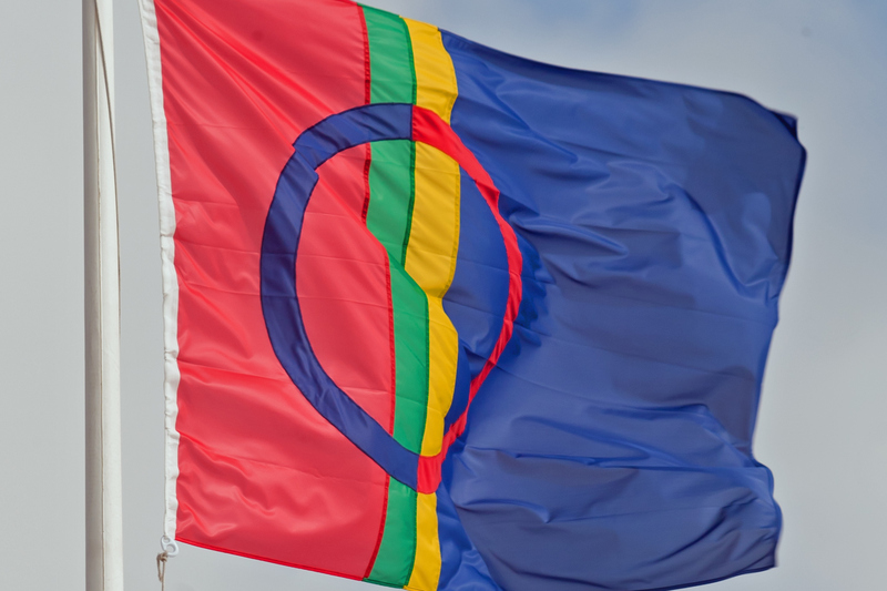 Samiska flaggan vajar på en flaggstång mot en halvklar himmel.