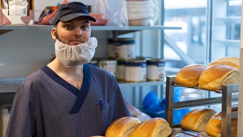 Han man håller i en plåt med bröd i köksmiljö.