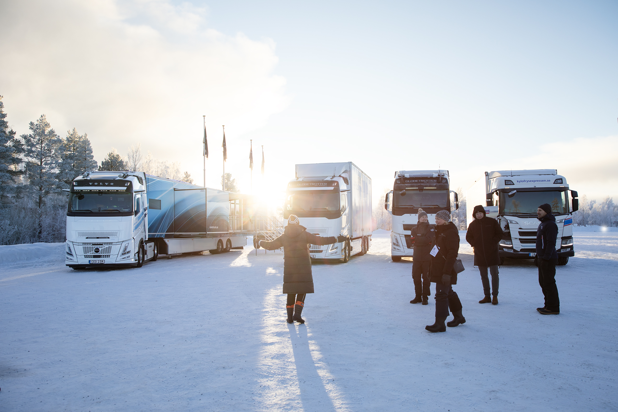 Besökare i sol sträcker ut armarna framför tunga fordon.