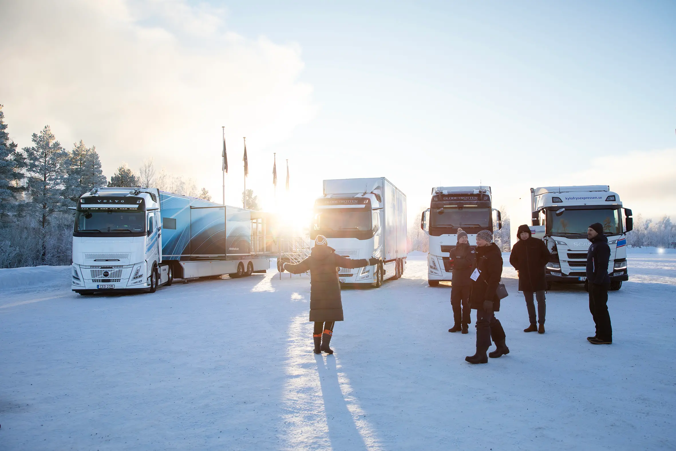 Besökare i sol sträcker ut armarna framför tunga fordon.