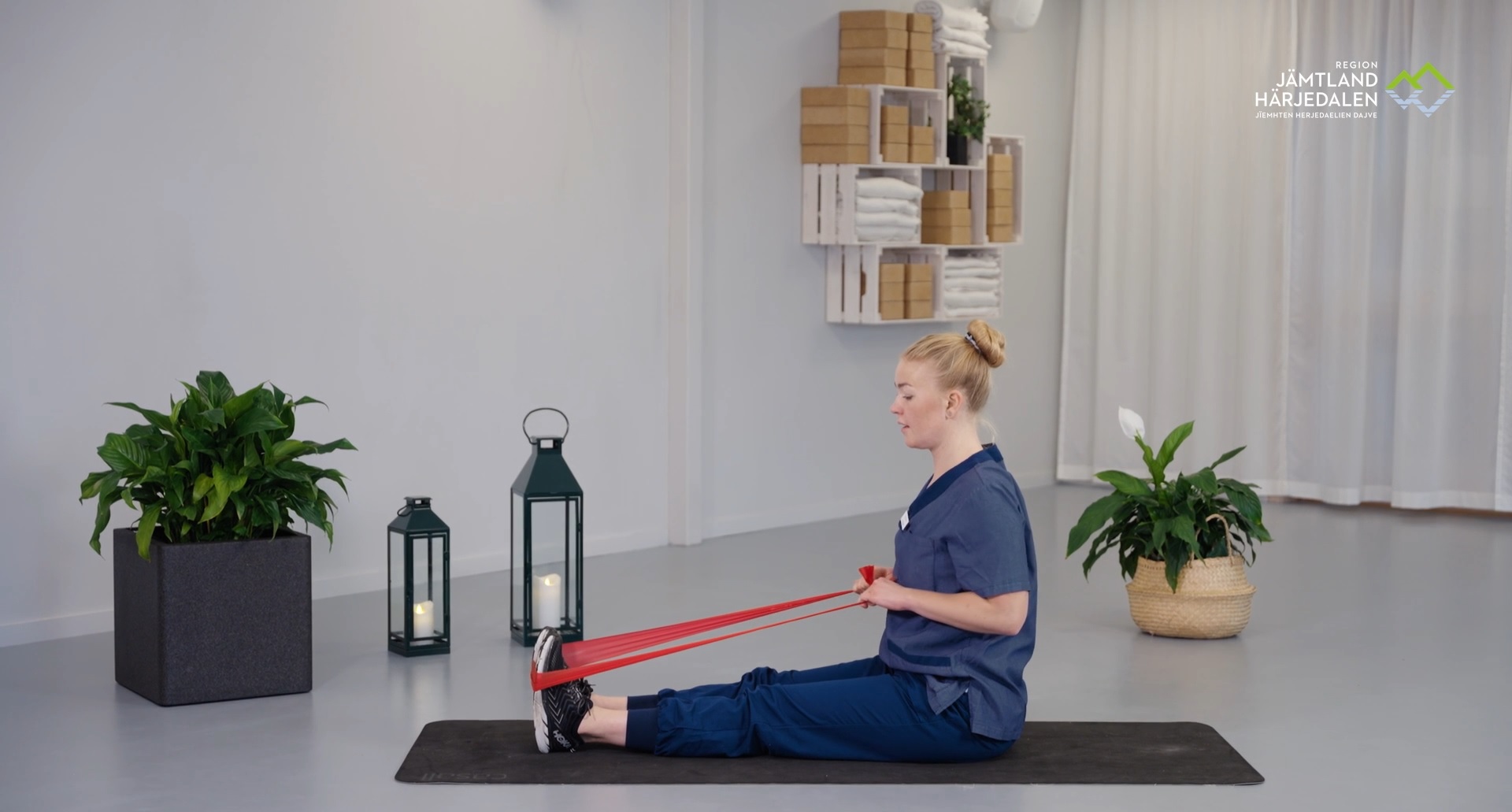 Vårdpersonal sitter på golvet och visar träningsövning med gummiband.