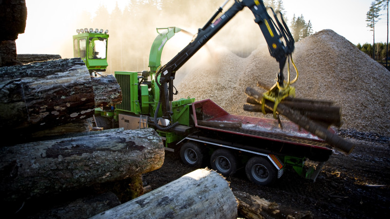Skogsmaskin lastar timmer på ett släp.