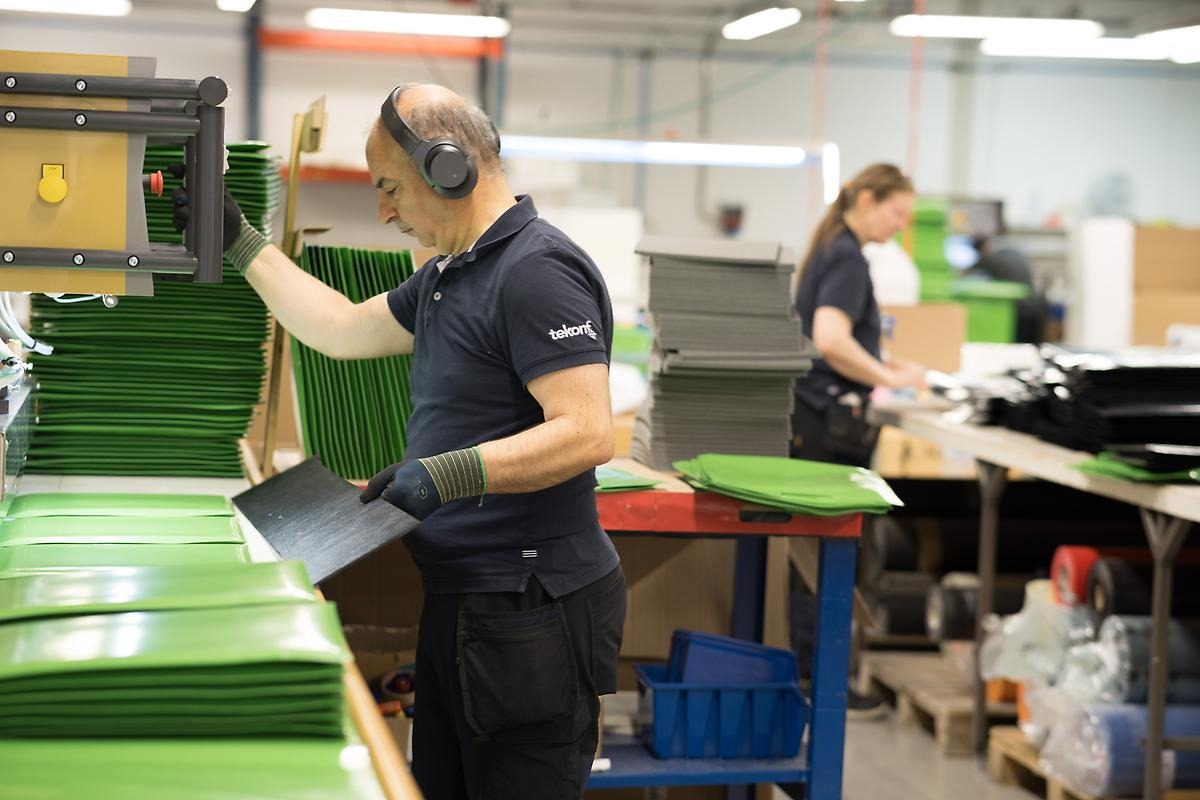 En fabriksarbetare står vid en maskin, i bakgrunden syns kollegor vid fler maskiner.