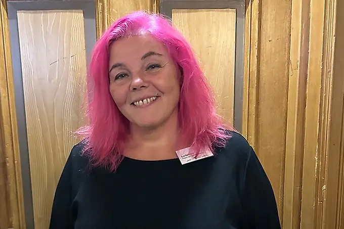 En rosahårig person ler brett mot kameran