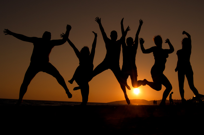 Silhuetterna av sju lyckliga personer som gör ett glädjeskutt i motljus under solnedgång.