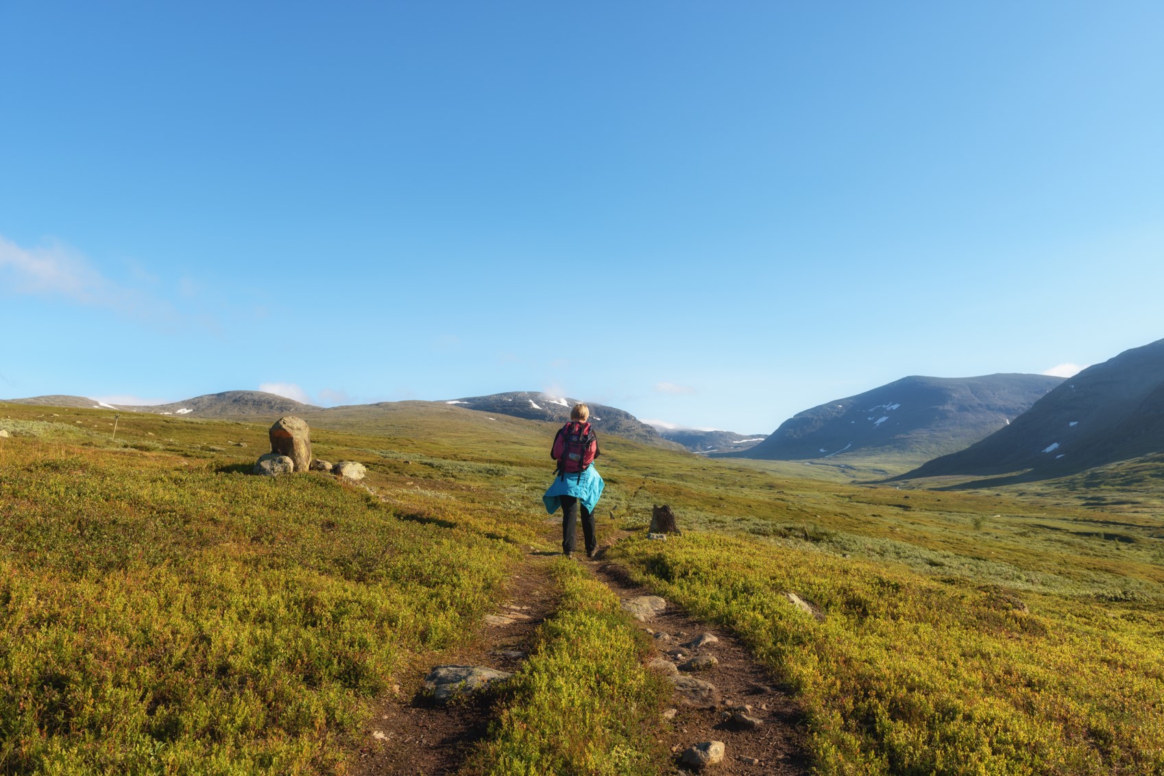 En person som går längs en stig på fjället. Blå himmel i bakgrunden. 