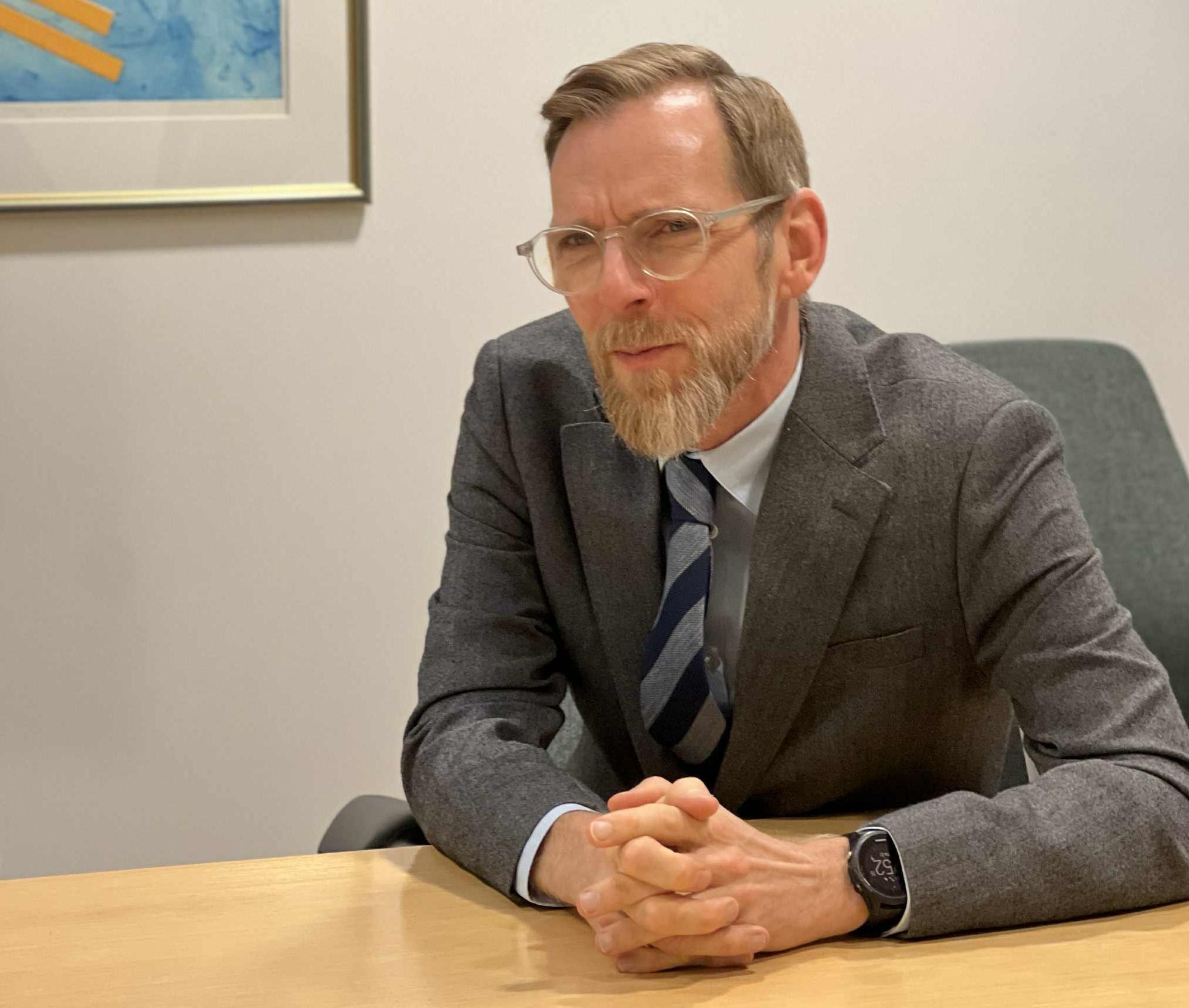 En man sitter vid ett skrivbord med knäppta händer och blicken riktad över bordet.