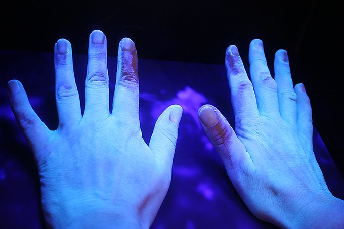 Ett par kvinnohänder i ultraljudsljus.Ljuset avslöjar de partier på händerna som inte desinficerats korrekt.