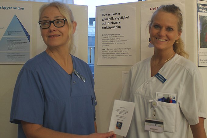 Två kvinnliga sjuksköterskor står tätt ihop framför informationsskärmar om handhygien