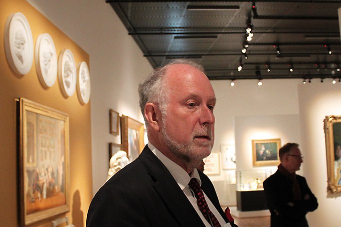En kostymklädd man står i profil inne i museet och berättar om konsten