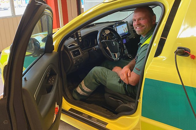 En person i uniform tittar ut från förarplats i en ambulans. Personen ler in i kameran