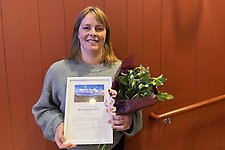 Porträttbild på en kvinna som håller i ett diplom och blommoer.