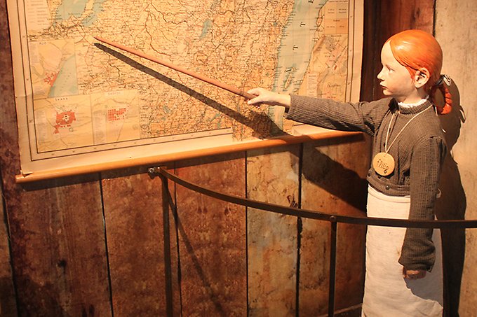 En flicka som pekar med en pinne på en karta. 1800-talsmiljö skolan