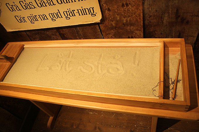 En träbänk med sand i för stavningsträning förr i tiden