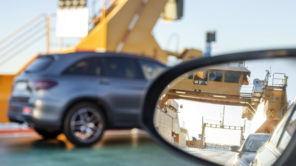 Detaljbild av en färja fotograferad genom en bilruta. En annan bil och en sidospegel syns också. 
