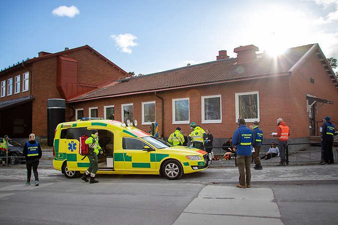 en ambulans står parkerad utanför en skola, ambulanspersonal går omkring utanför