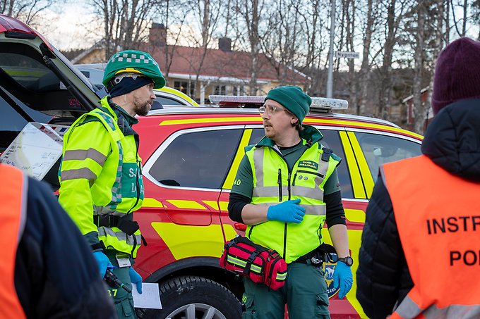 två ambulanssjuksköterskor pratar med varandra framför en röd ledningsbil från räddningstjänsten