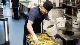 En man i köksmiljö sprinklar koriander över enchiladas.