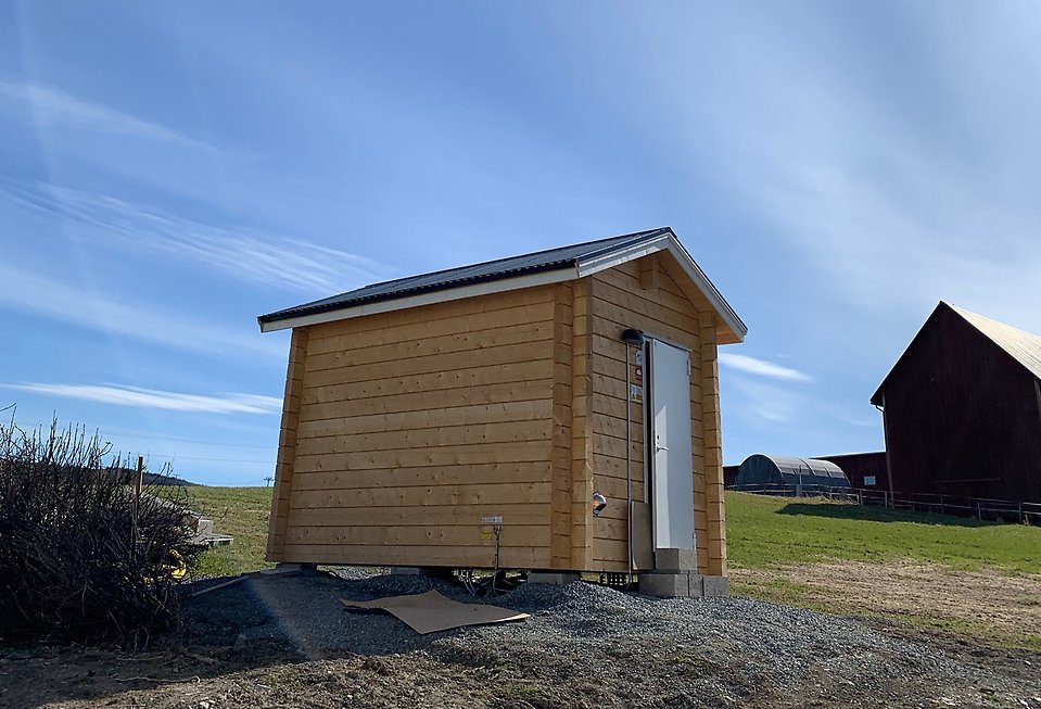 Ett litet timmrat husmed en klarblå himmel i bakgrunden. 