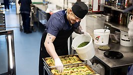 En man i köksmiljö sprinklar koriander över enchiladas.