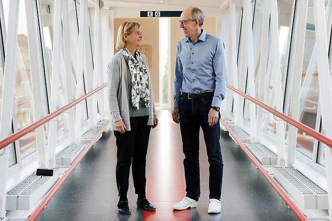 en kvinna och en man står i en korridor med glasväggar och tittar på varandra