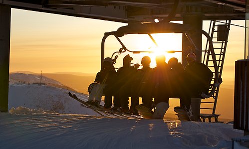 En sittlift med sex personer i motljus och solnedgång, som precis ska gå av liften.