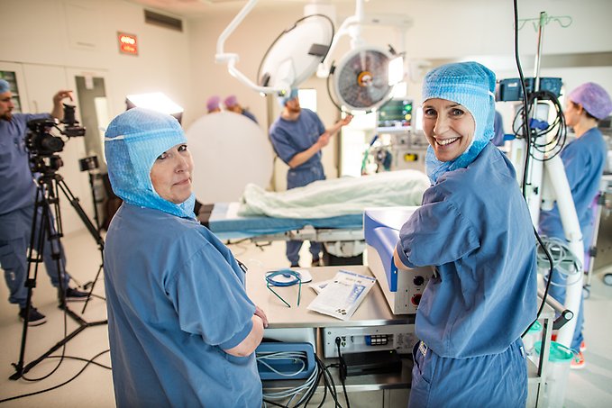 två kvinnor klädda i vårdkläder för en operation står i en operationssal